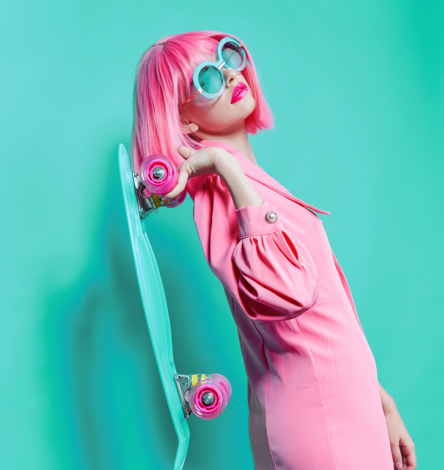 a woman wearing all pink in a pink costume party wig holding a skateboard 